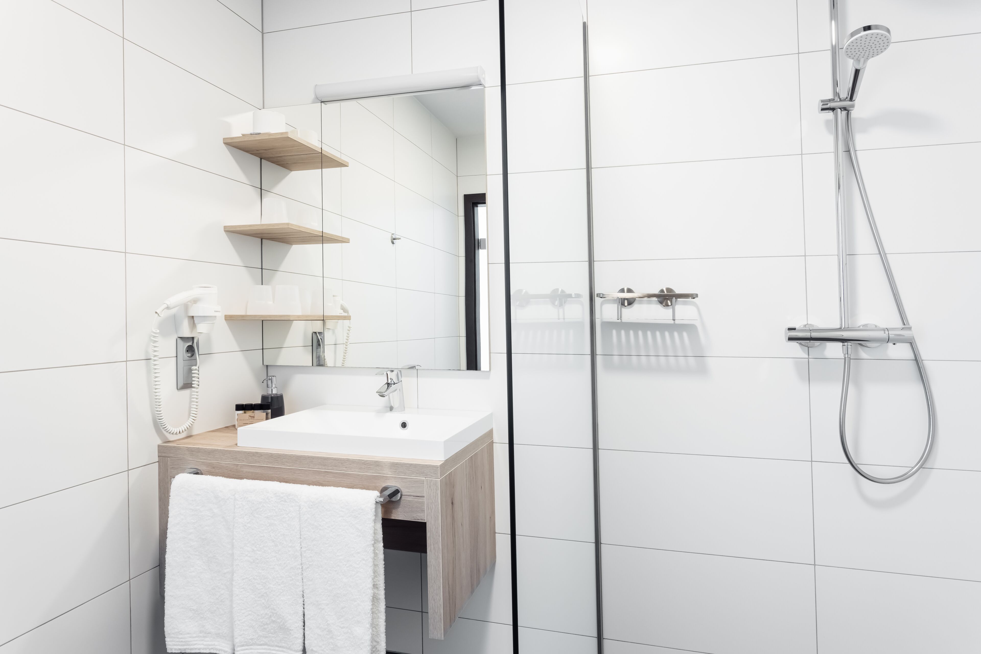 Ein modernes Badezimmer mit einem weißen Waschbecken, einer Holz-Kommode und einer Duschkabine aus Glas.