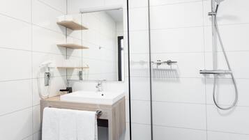 Ein modernes Badezimmer mit einem weißen Waschbecken, einer Holz-Kommode und einer Duschkabine aus Glas.
