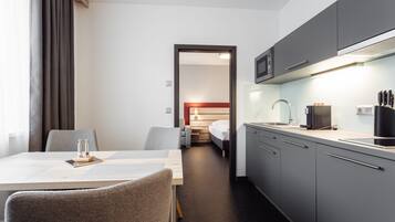 Compact hotel room with a kitchenette, dining area, and comfortable bed.