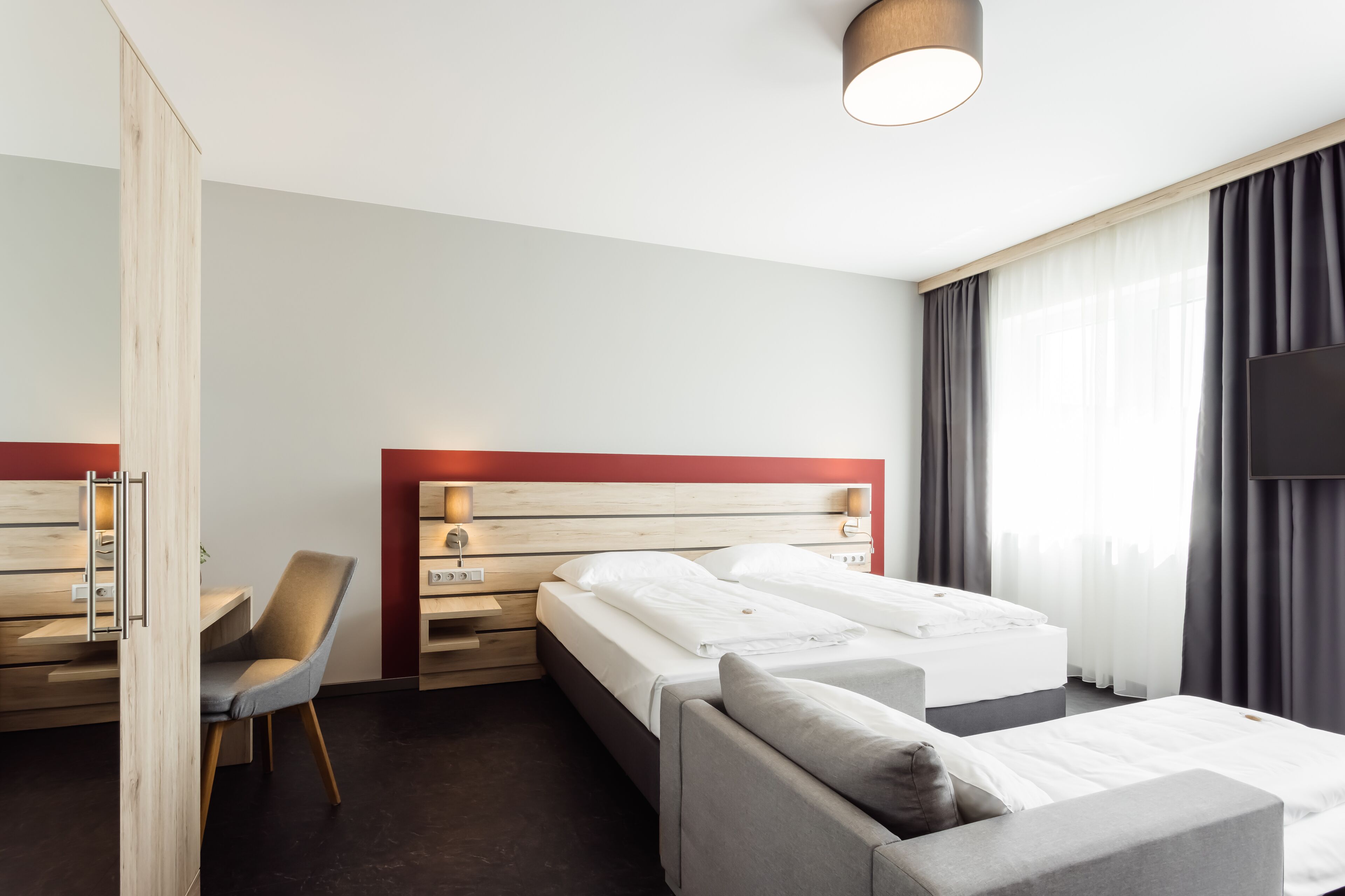 A hotel room with a bed, a desk, a chair, and a TV.