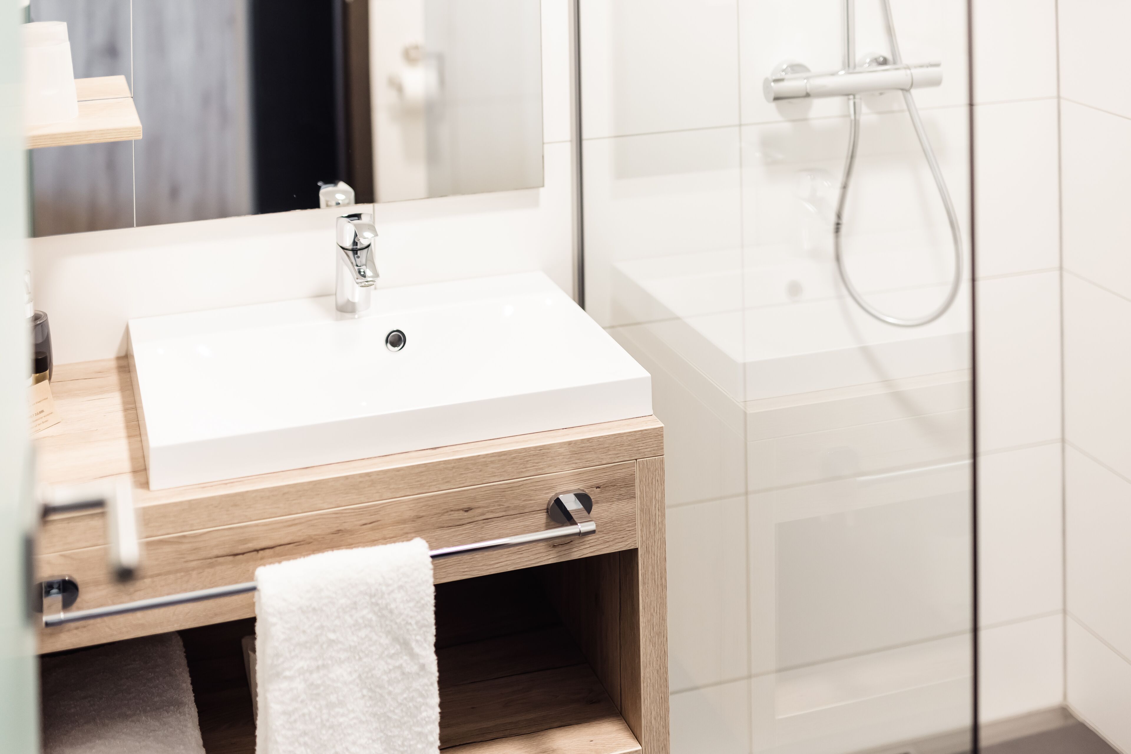 Een moderne badkamer met een witte wastafel, een houten wastafelmeubel en een douchecabine van glas.