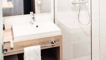 Een moderne badkamer met een witte wastafel, een houten wastafelmeubel en een douchecabine van glas.