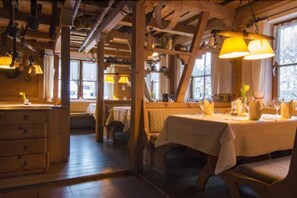 Un interior rústico de madera con vigas a la vista, una zona de comedor con una mesa dispuesta para dos personas y un banco.