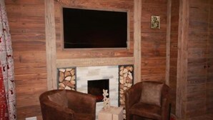 A log cabin interior with a fireplace, two leather armchairs, and a mounted television. - Hotel Höhengasthof Grüner Baum (Feldberg)