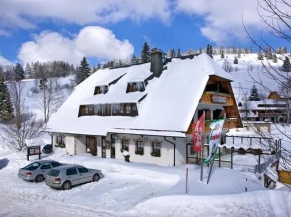 Un edificio cubierto de nieve con techo inclinado, entrada visible y una bandera.