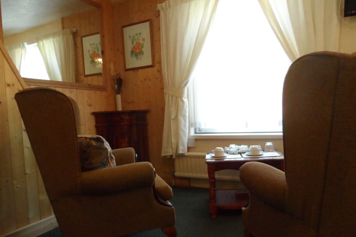 A room with two armchairs, a wooden table with tea sets, and a window with curtains.