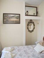 Un dormitorio con una cama, un cuadro de un paisaje enmarco y un espejo con un marco ornamentado.