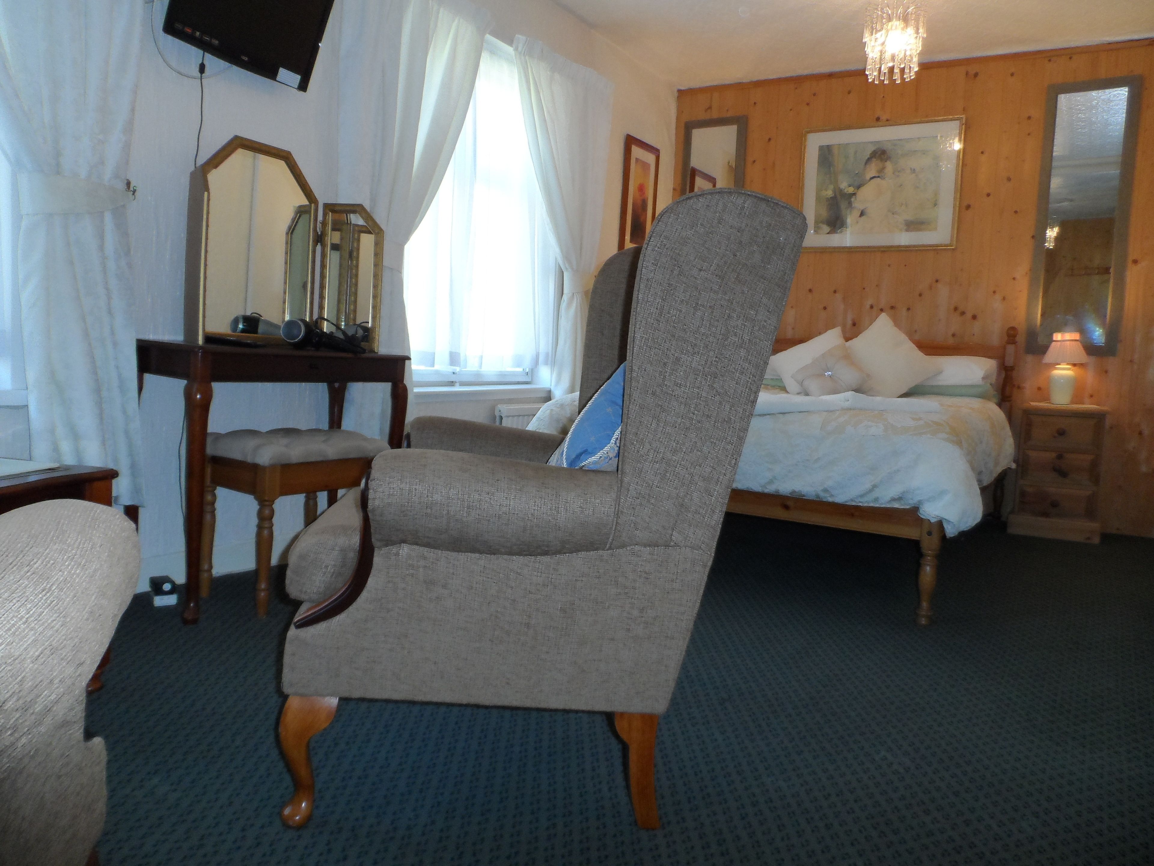 A bedroom with a bed, a chair, a desk, a mirror, and a television.
