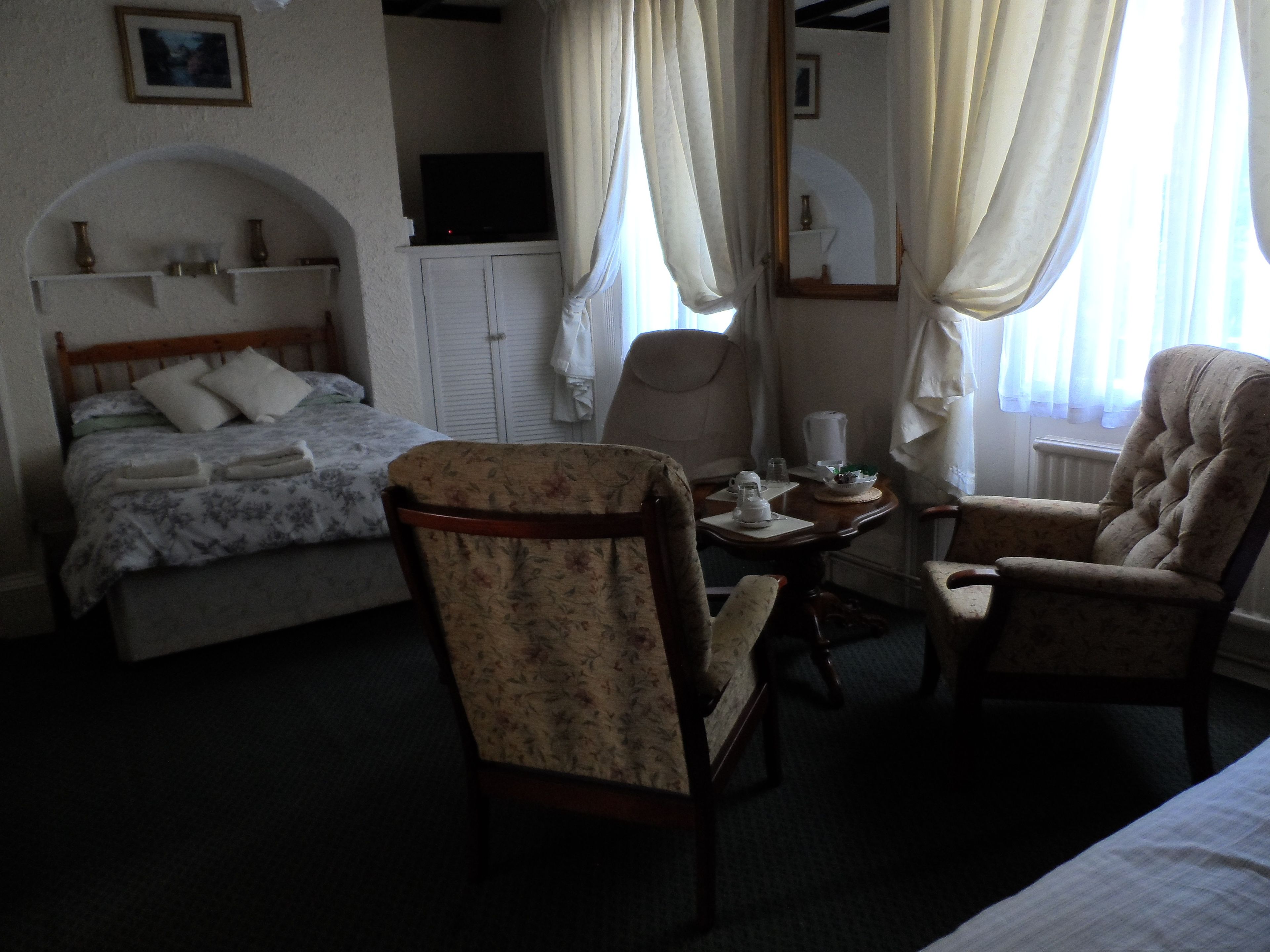 Een hotelkamer met een bed, twee stoelen, een klein tafeltje met een theepot en een televisie op een kast.