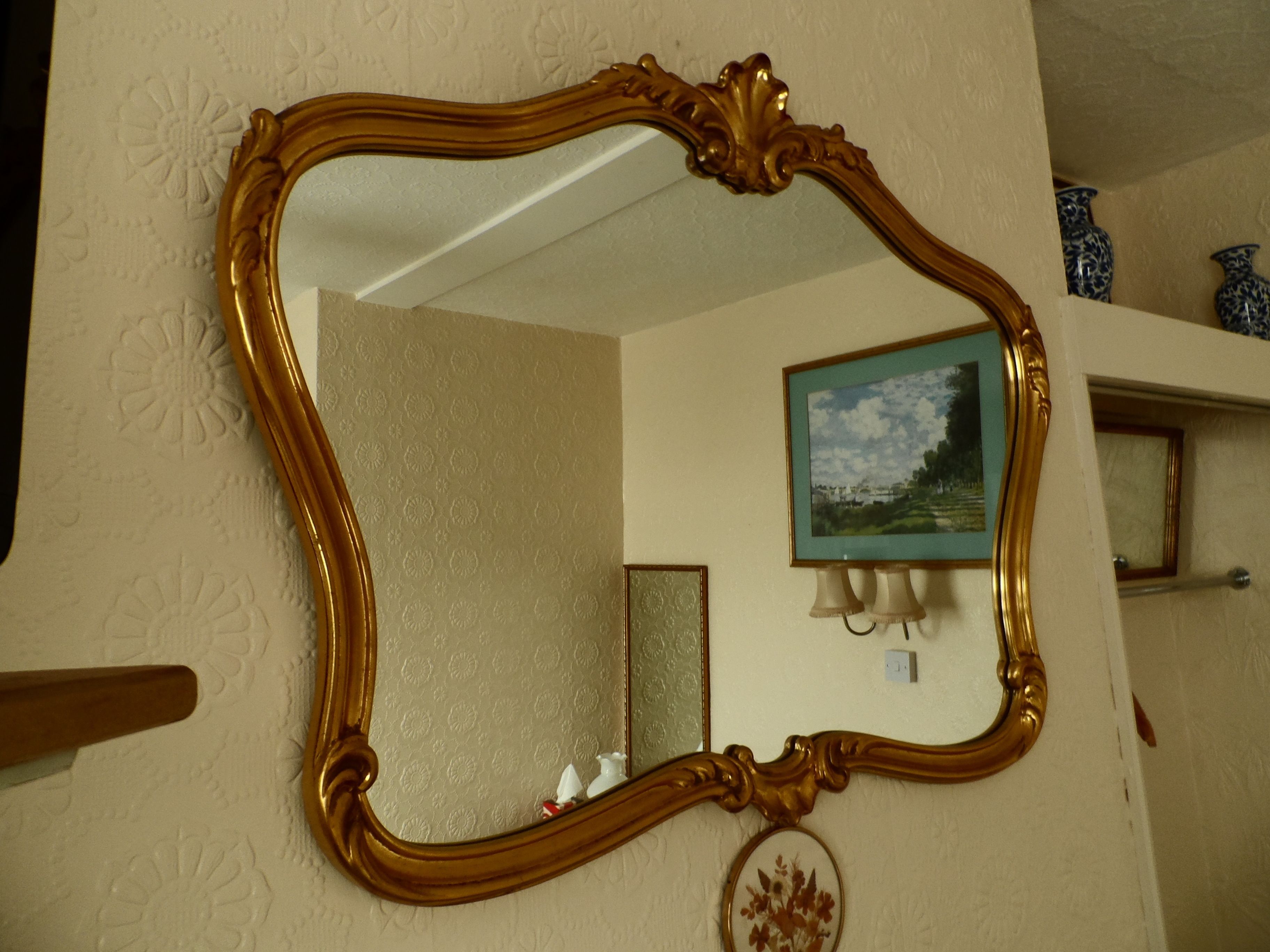 Un espejo con un marco dorado ornamentado en la pared.