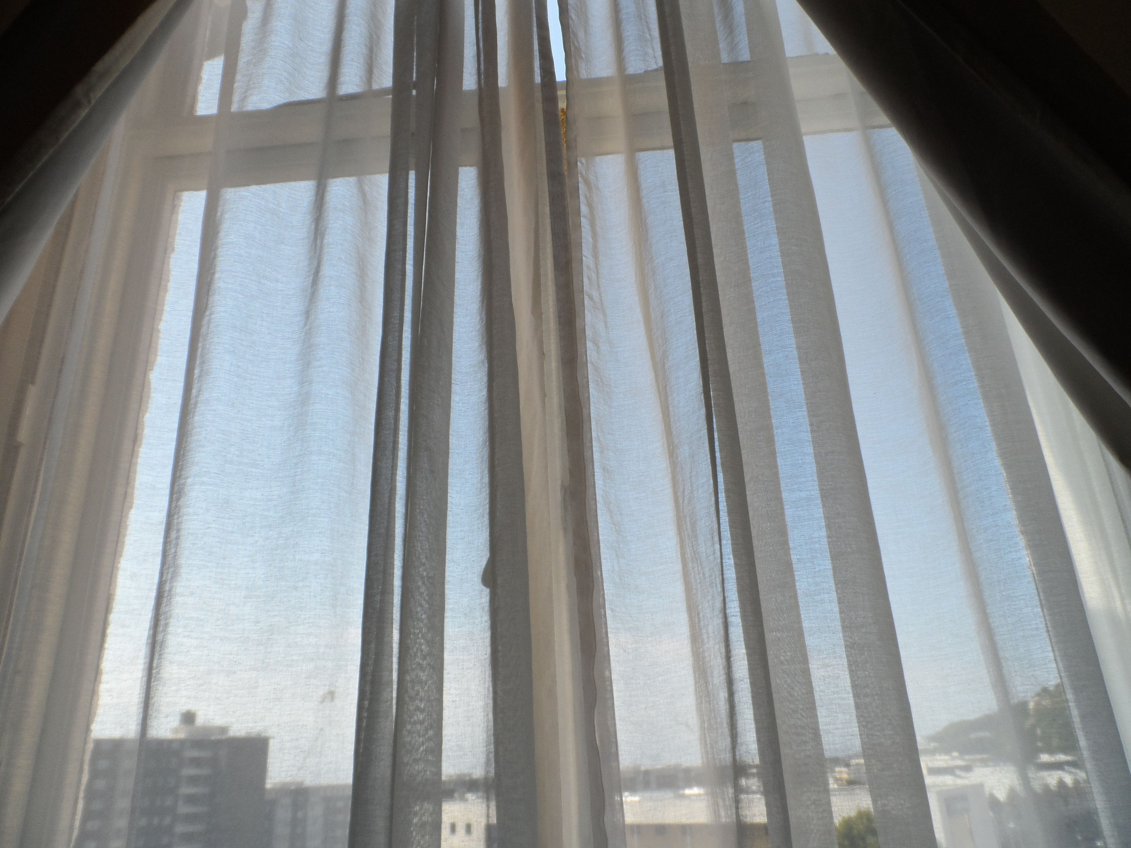 A view through sheer curtains with a cityscape visible in the background.