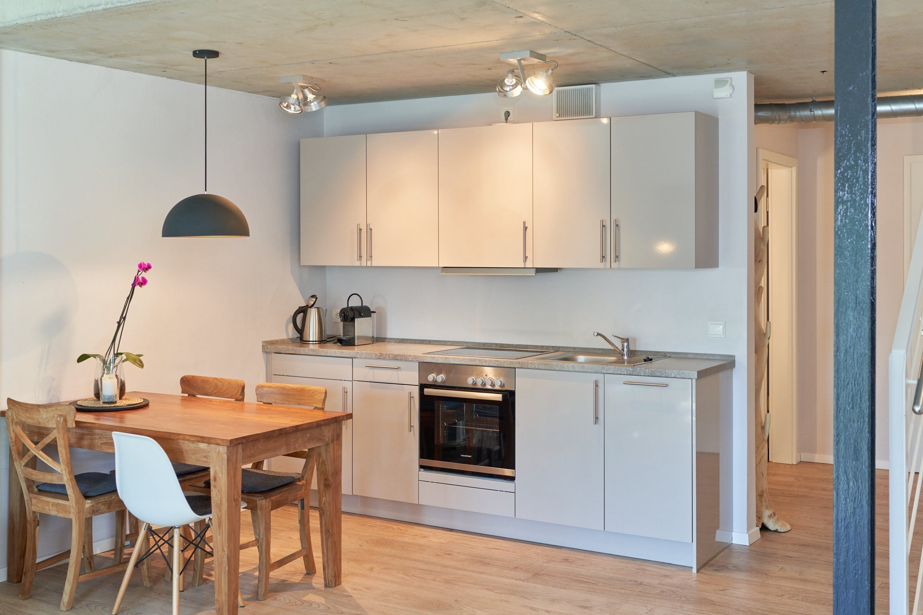 Une cuisine moderne avec des meubles blancs, une table à manger en bois et un four encastré.