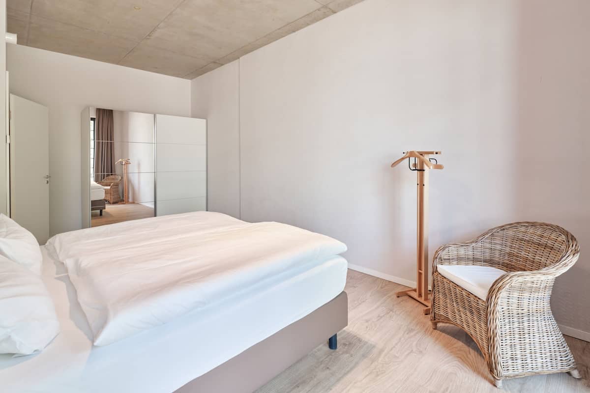 A modern bedroom with a large bed, a wicker chair, and a floor lamp.