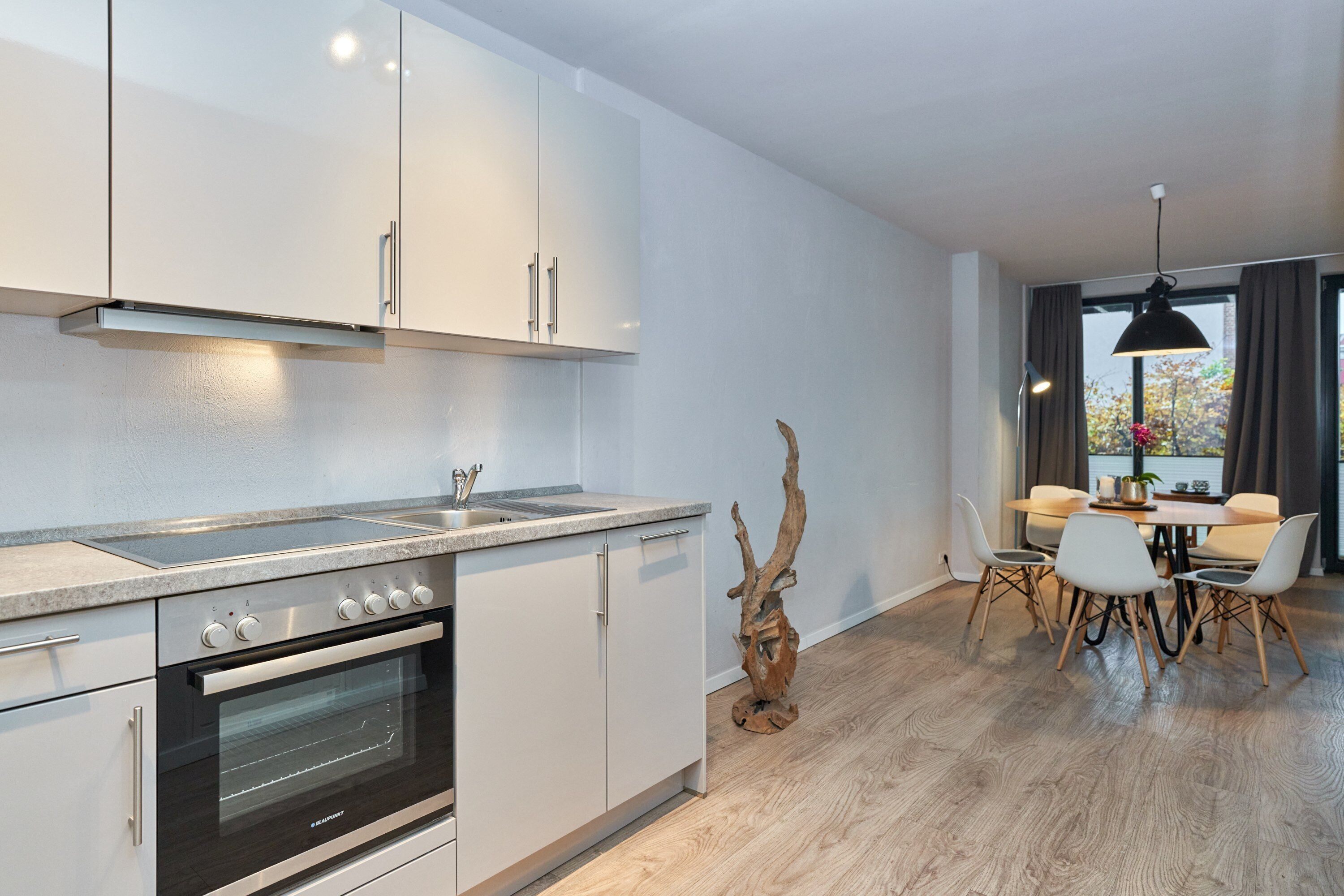 Eine moderne Küche mit weißen Schränken, einem eingebauten Backofen und einem Essbereich mit Tisch und Stühlen.