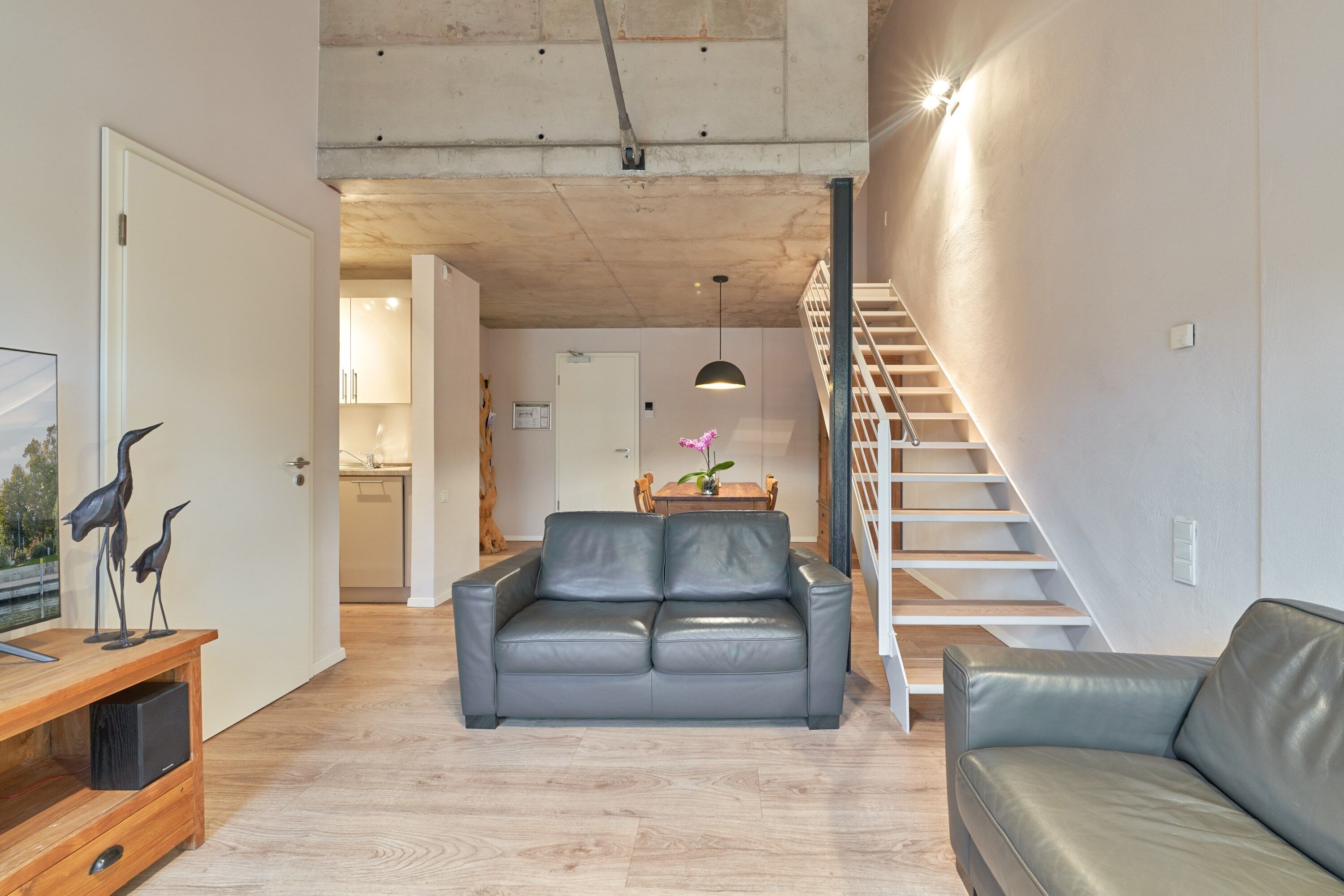 A spacious living area with a grey leather sofa, a wooden coffee table, and a staircase leading to an upper floor.
