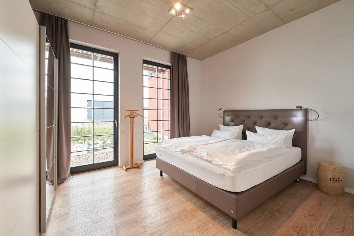 A bedroom with a large bed, a wooden floor, and a view through a window.