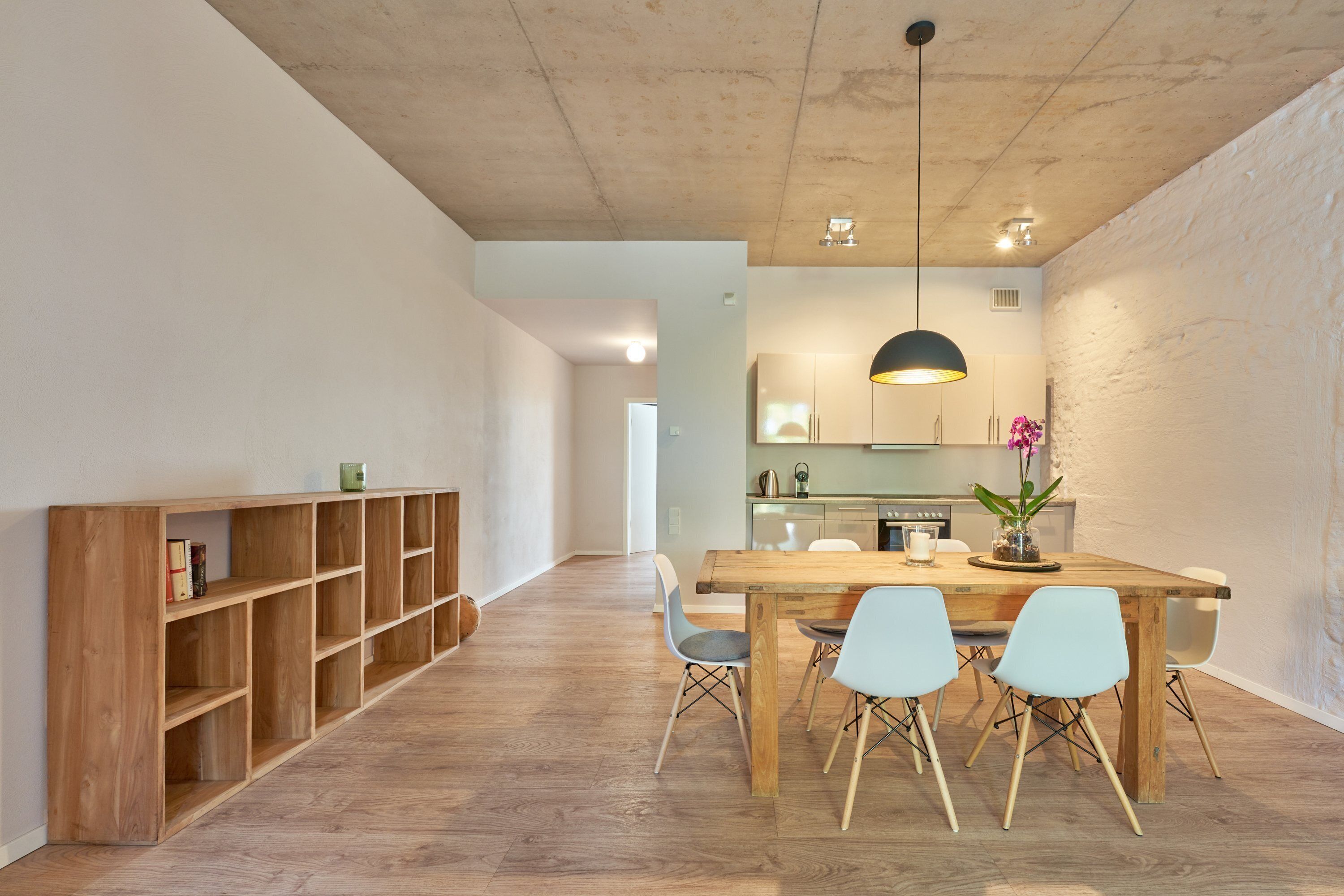Una cocina moderna con una mesa y sillas de madera, una estantería empotrada y una lámpara colgante.