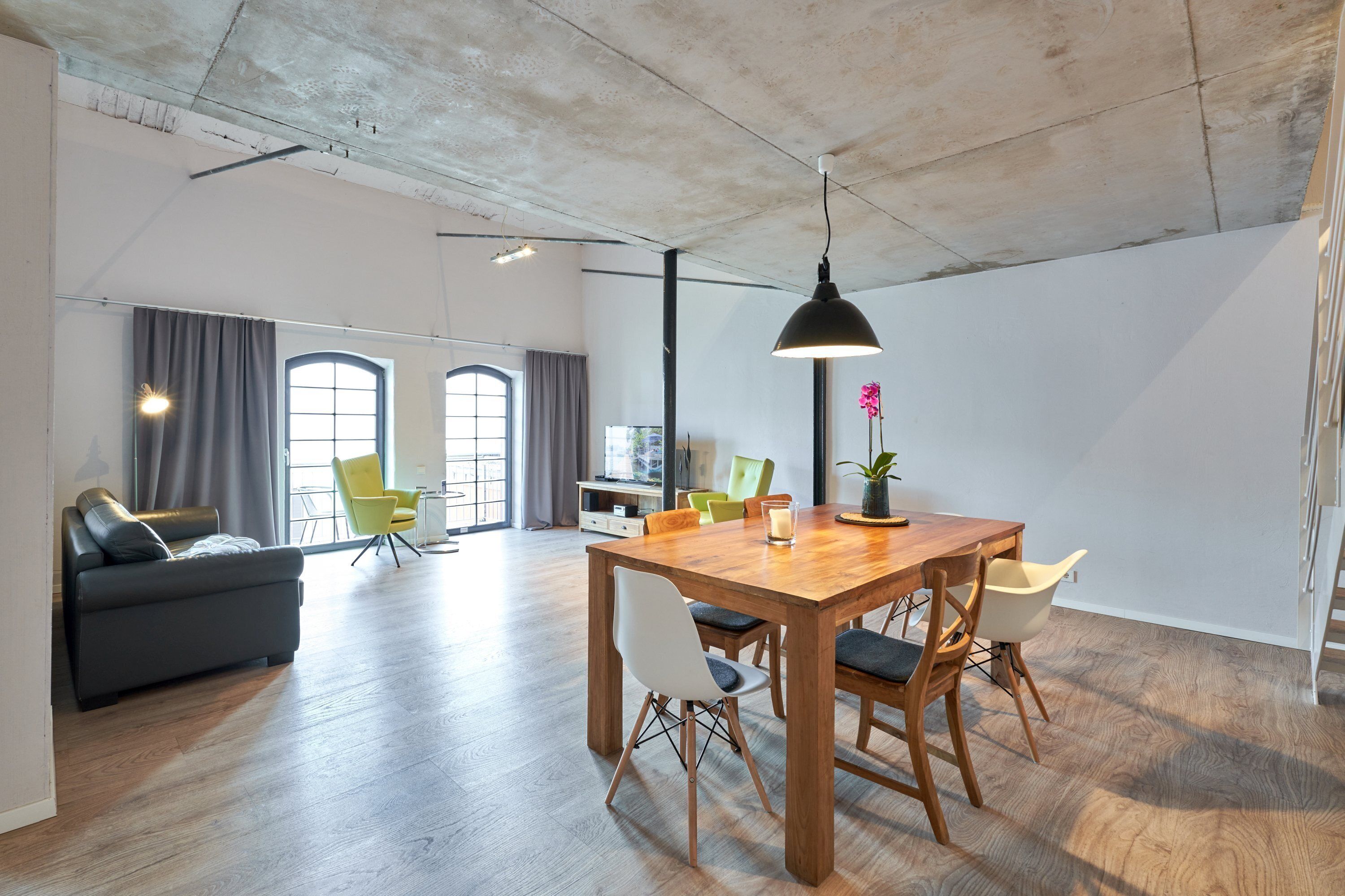 Un vaste espace de vie comprenant une table à manger en bois, des chaises, un canapé et une grande fenêtre agrémentée de rideaux.