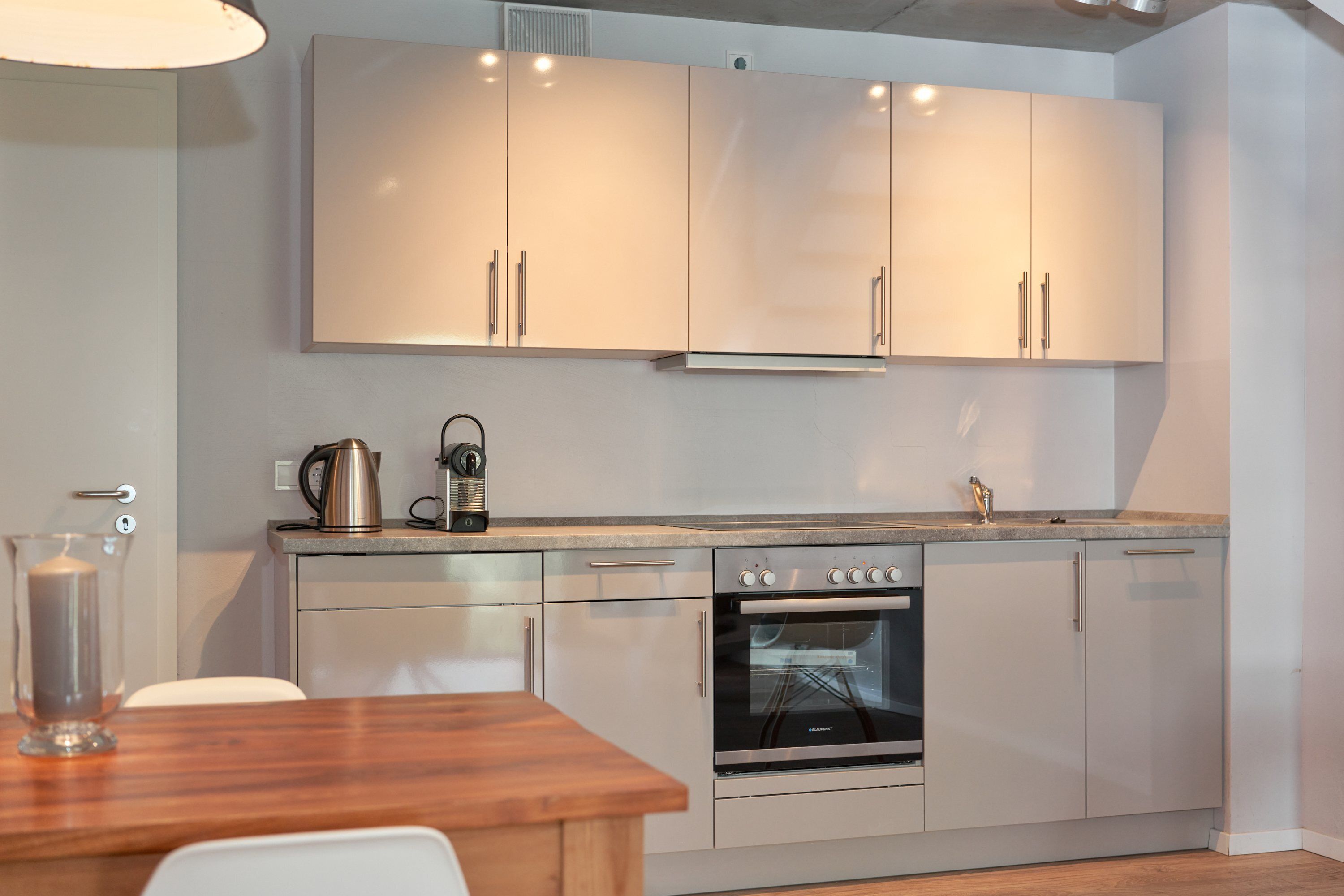 Una cocina moderna con armarios blancos, horno empotrado y cafetera en la encimera.