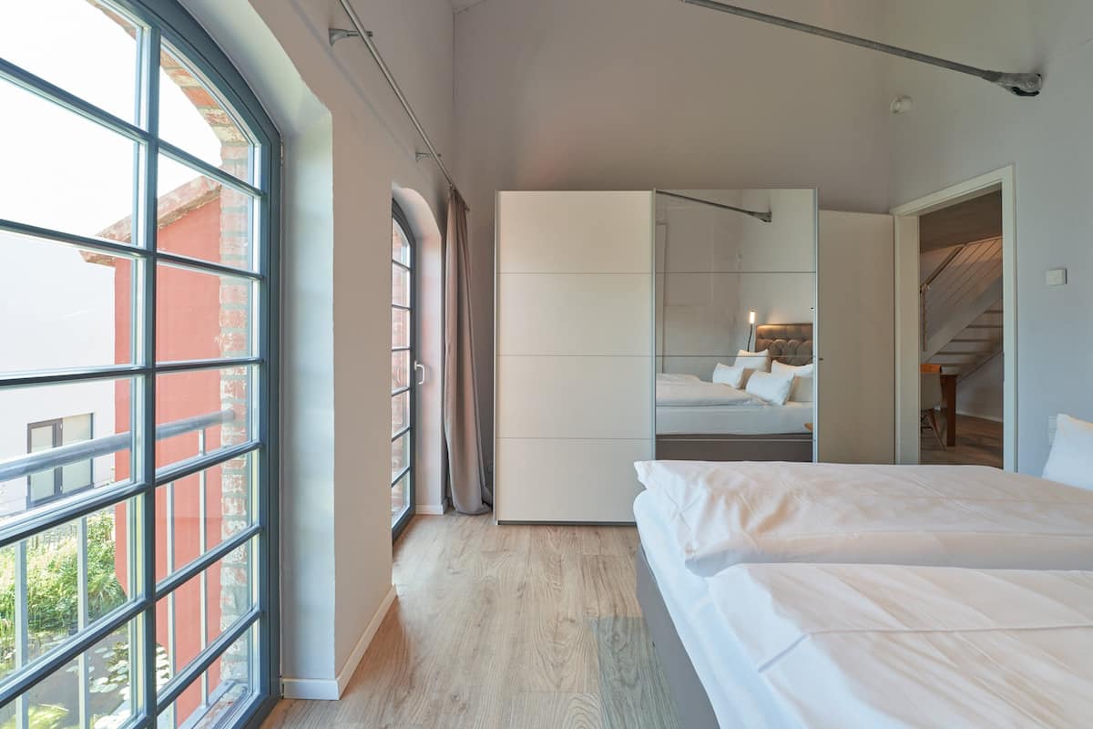 A modern bedroom with a large window, a wardrobe, a bed, and a staircase.