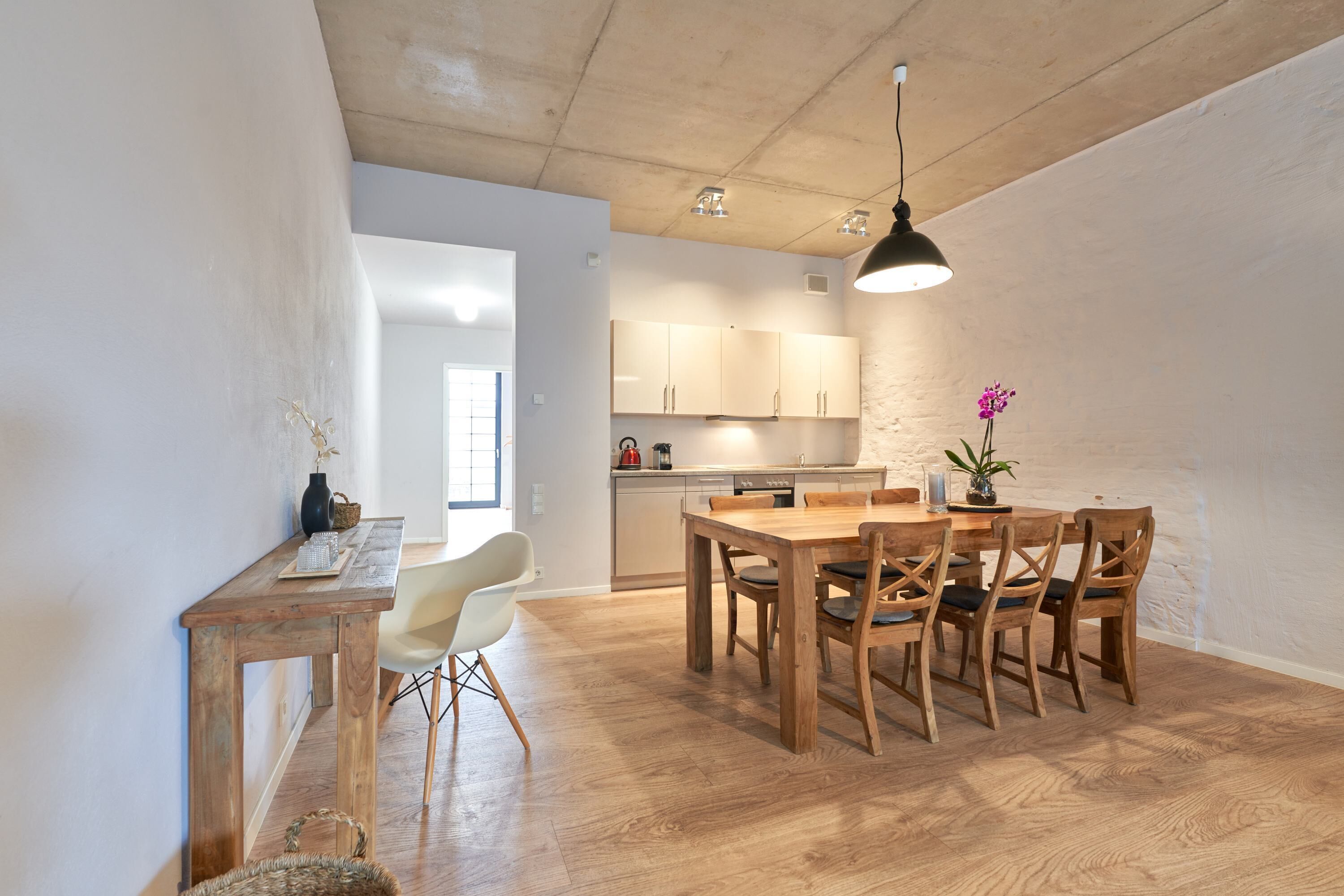 A modern kitchen with wooden cabinets, a dining table with chairs, and a hanging light fixture.
