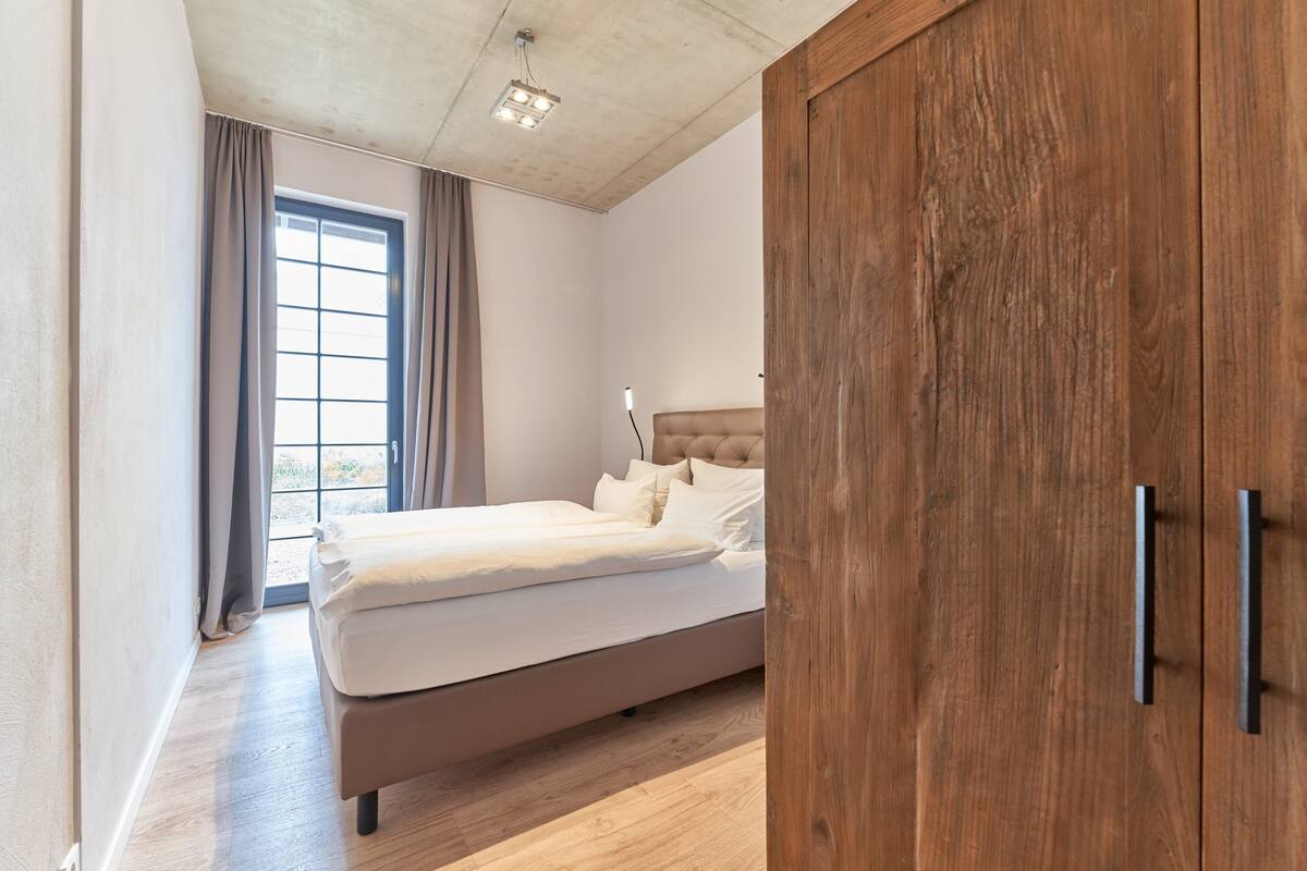 A bedroom with a large bed, wooden wardrobe, and a window with curtains.