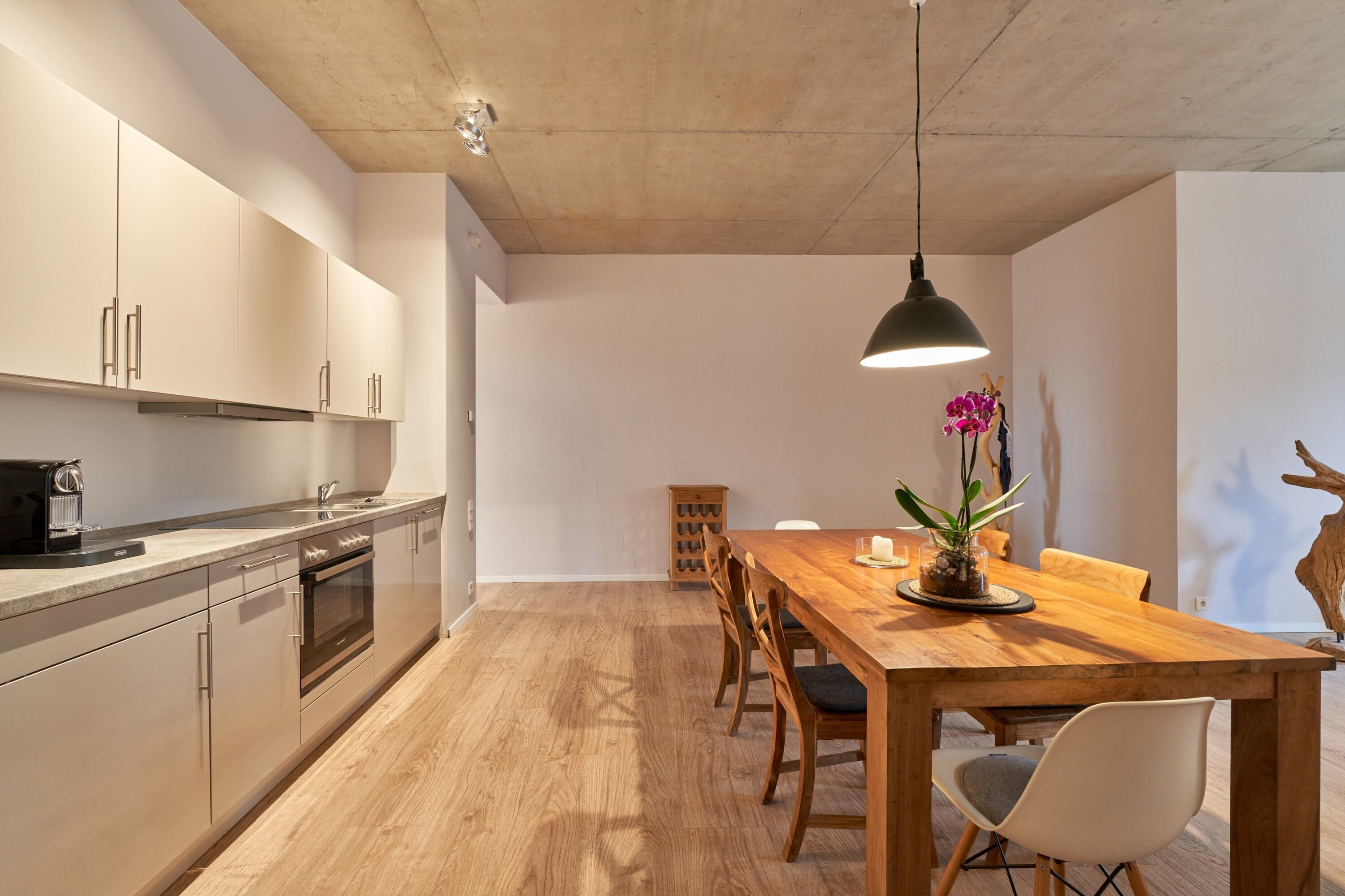 Une cuisine moderne avec une table et des chaises en bois, un four encastré et un luminaire suspendu.