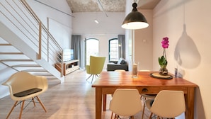 A modern interior with a wooden dining table, white chairs, a yellow chair, a staircase, and a view to a living area. - havelblau FERIENLOFTS (Brandenburg an der Havel)