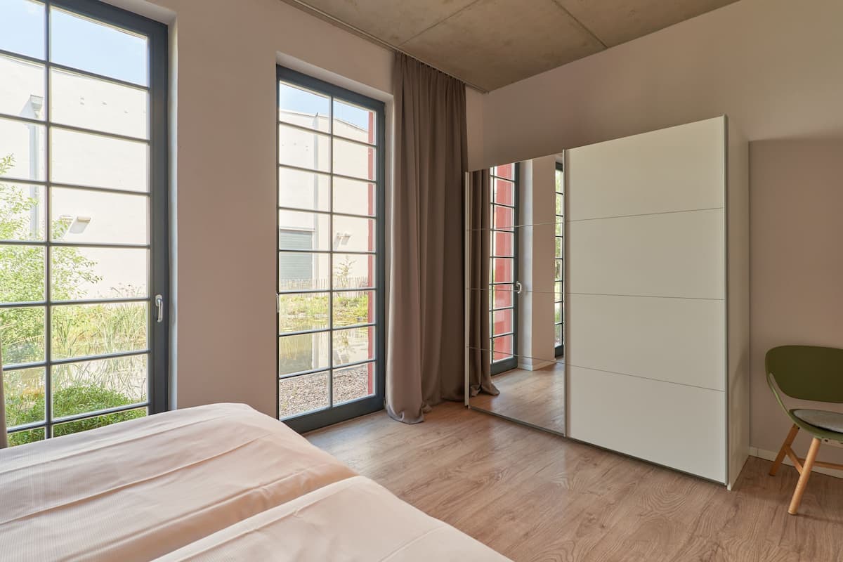 A modern bedroom with a large window, a bed, a wardrobe, and a chair.