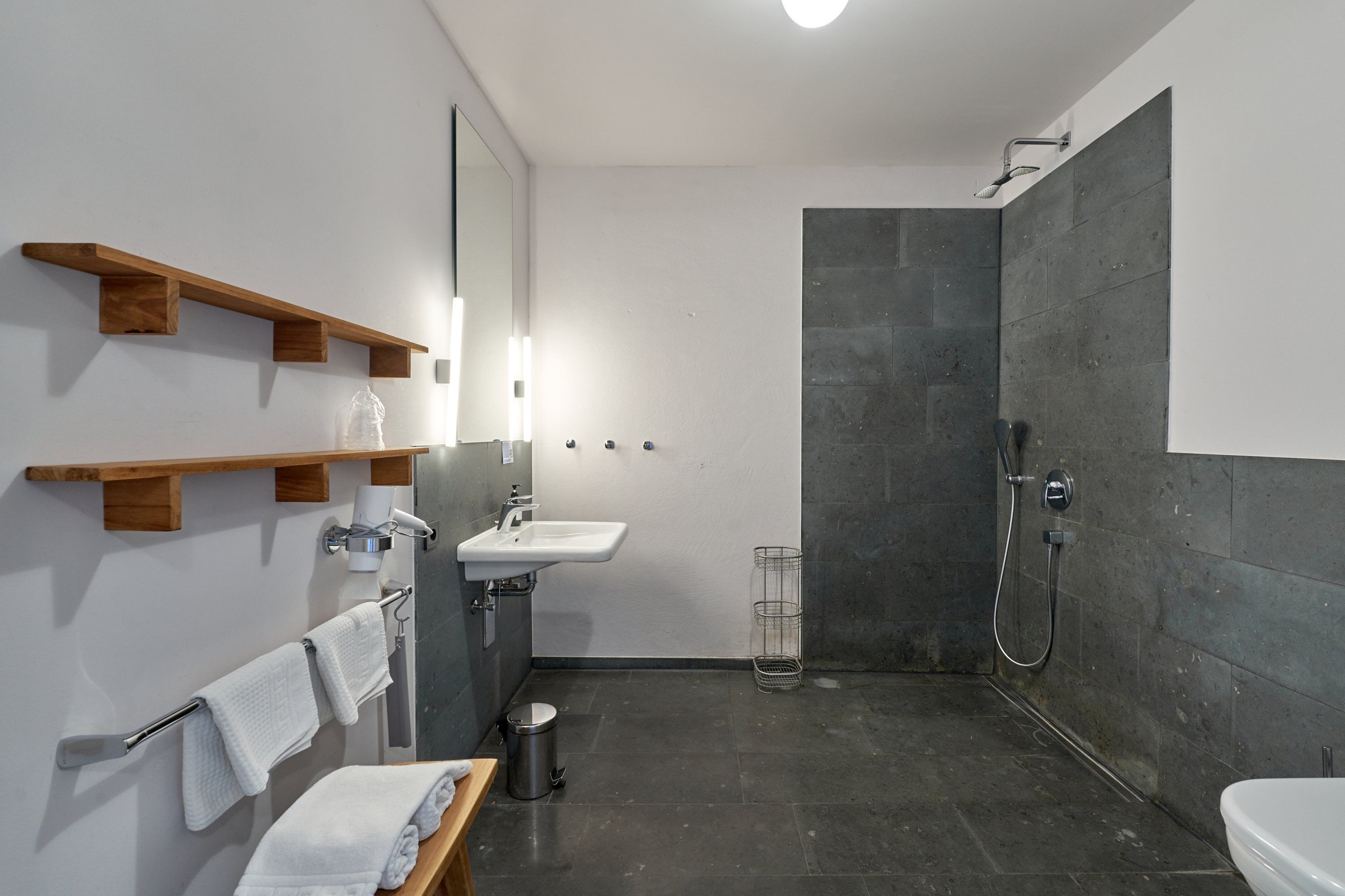 A modern bathroom with a shower, sink, and wooden shelves.