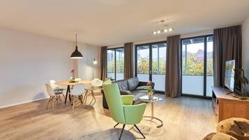 A modern living room with a dining area, large windows, and a view of trees outside.