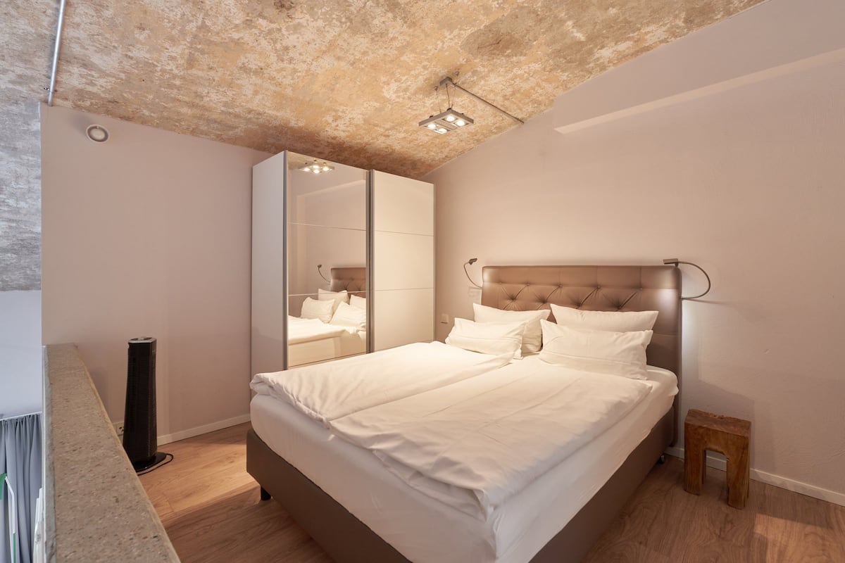 A modern bedroom with a large bed, a mirror, and a small stool.