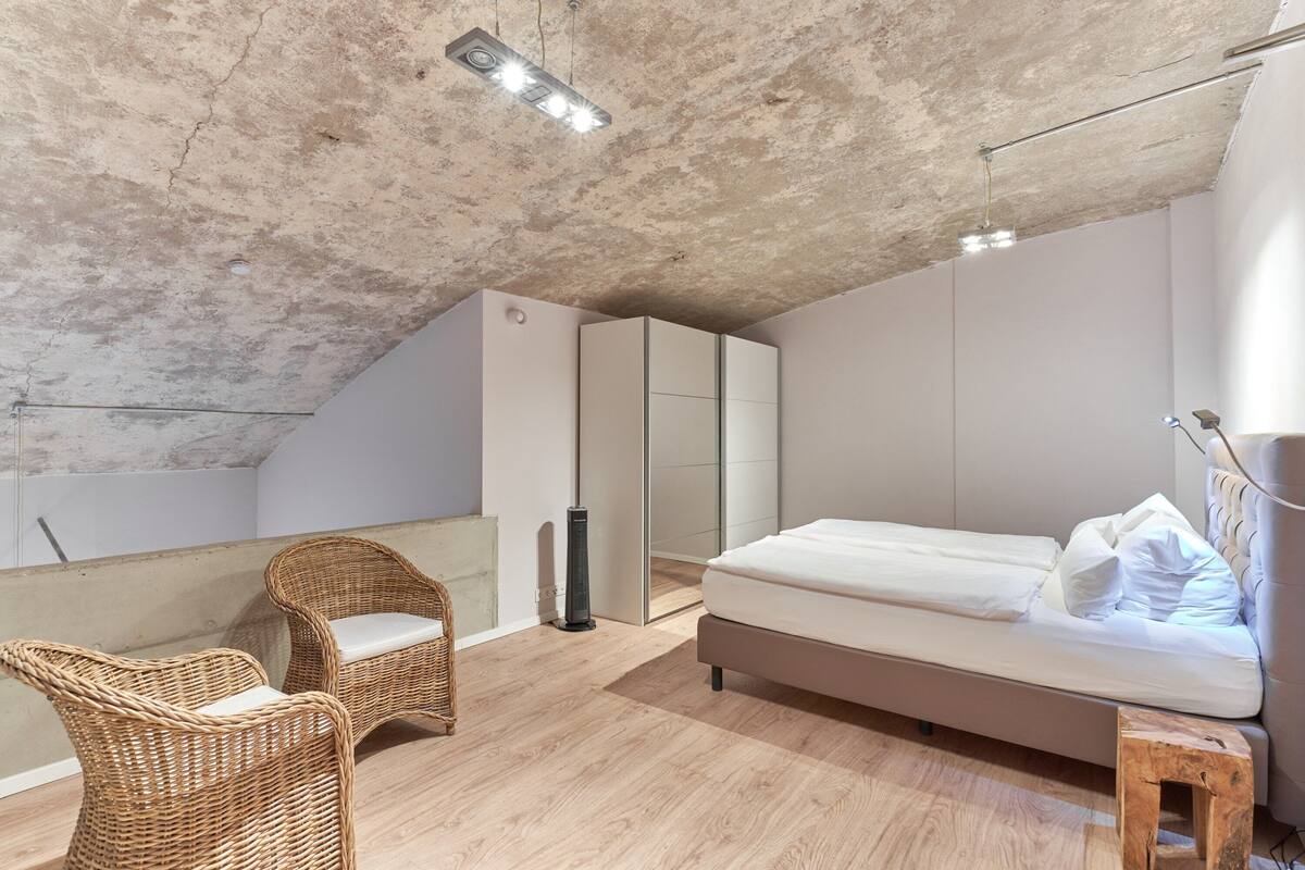 A bedroom with a bed, two wicker chairs, a wardrobe, and a heater.