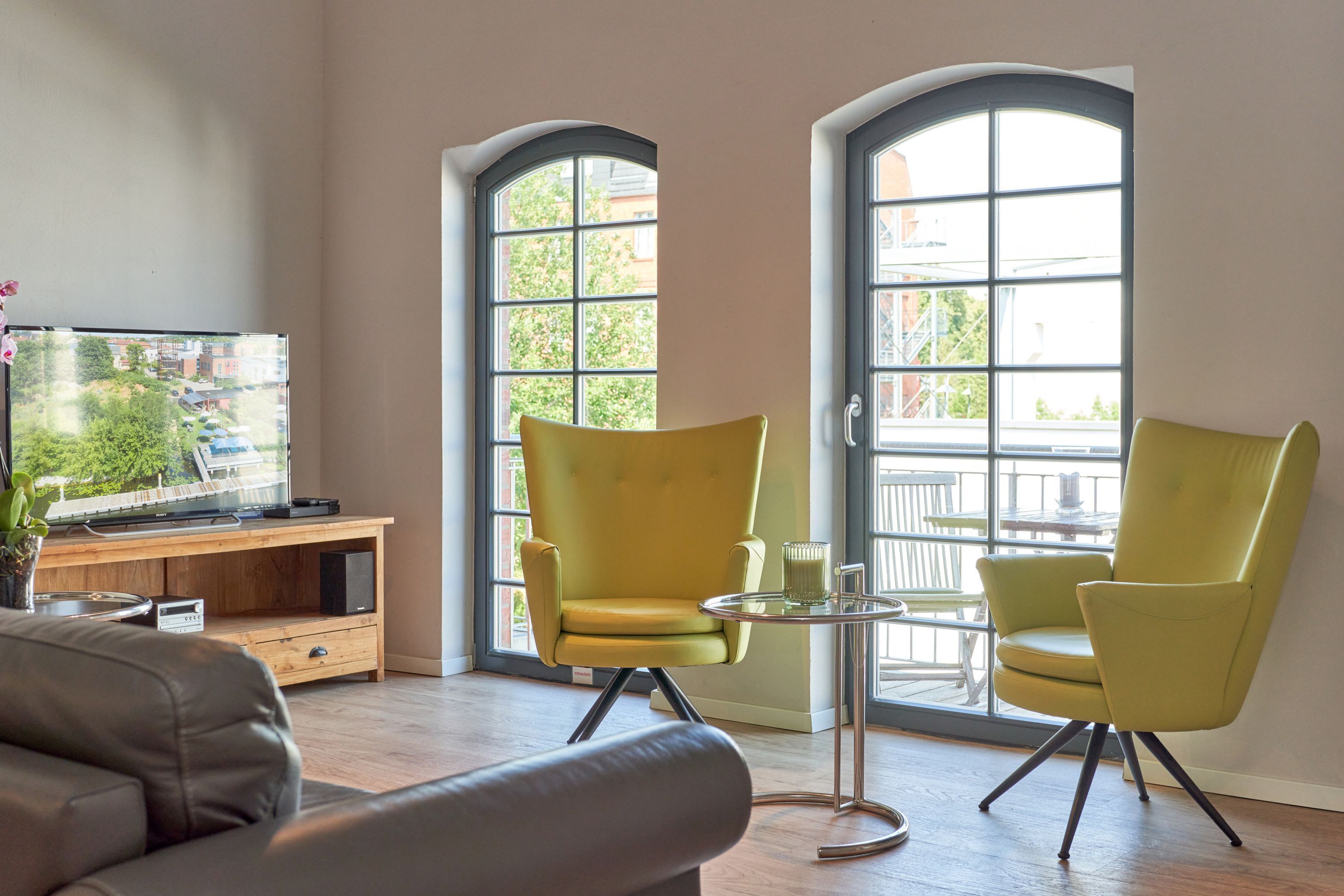 Una sala de estar moderna con un sofá, dos sillones amarillos, una mesa de centro de vidrio y un mueble de madera para televisión.