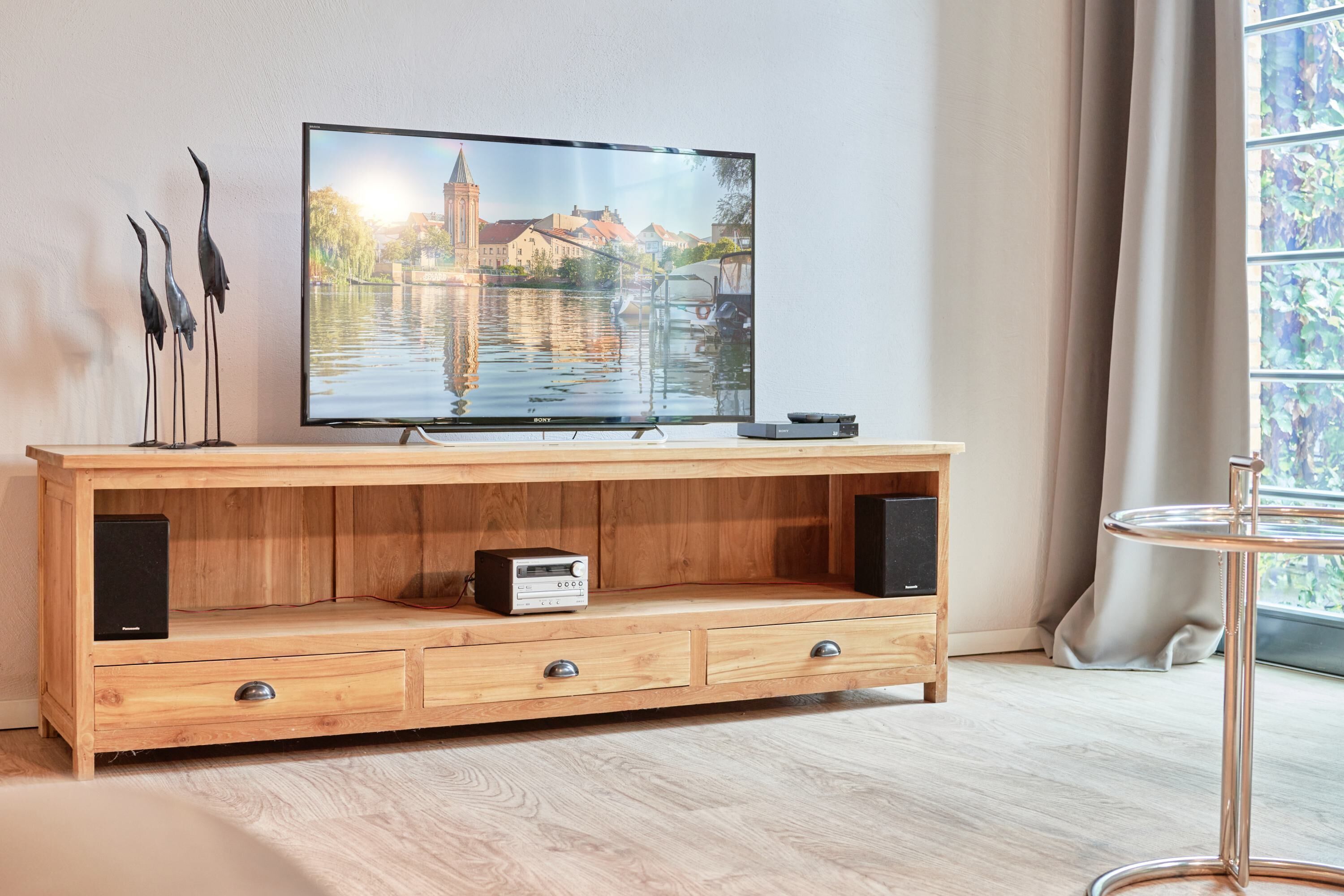 Un mueble bajo de madera para televisor con un televisor de pantalla plana mostrando un paisaje urbano, un altavoz pequeño y un cajón.