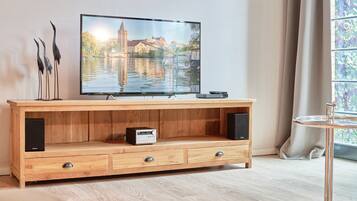 Un mueble bajo de madera para televisor con un televisor de pantalla plana mostrando un paisaje urbano, un altavoz pequeño y un cajón.