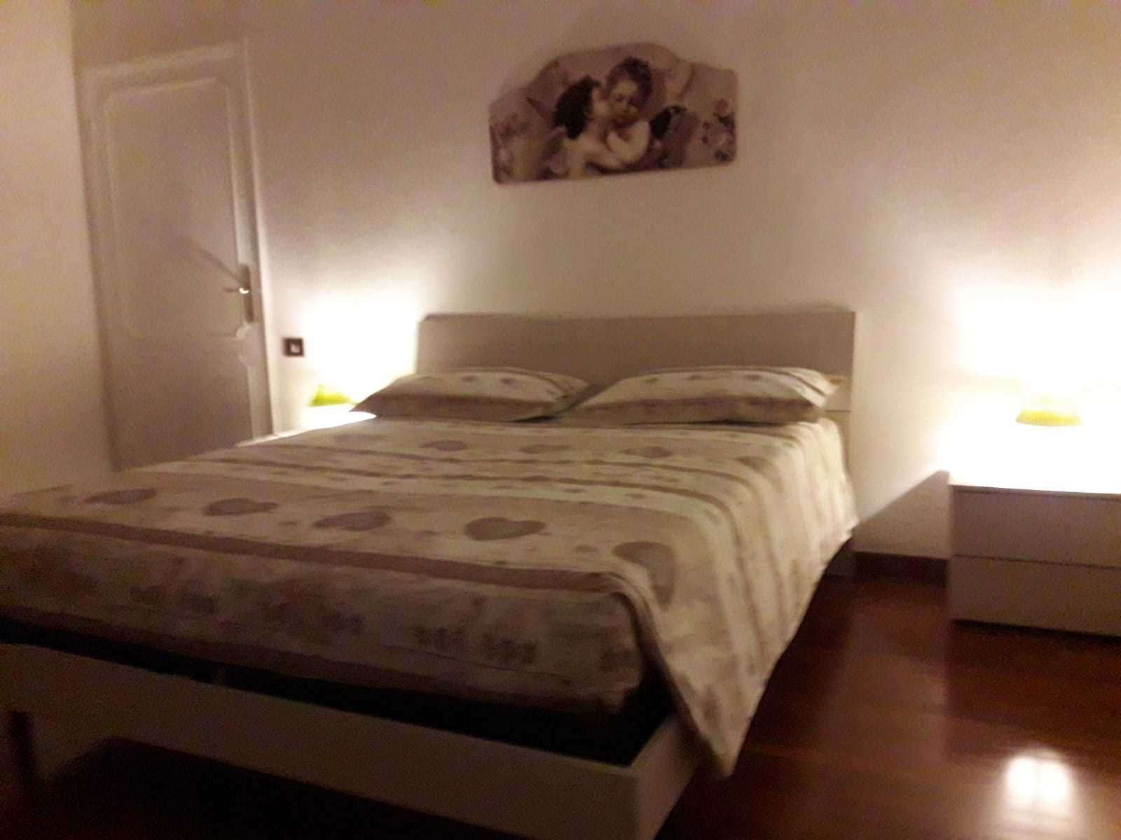 A bedroom with a bed, a nightstand, and a wall-mounted picture.