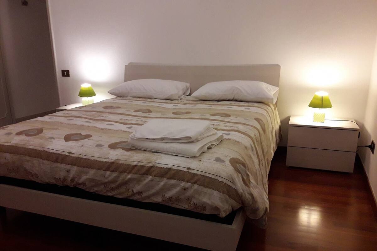 Un lit bien fait, avec une couvre-lit à motifs, deux lampes de chevet et une serviette pliée posée sur le lit.