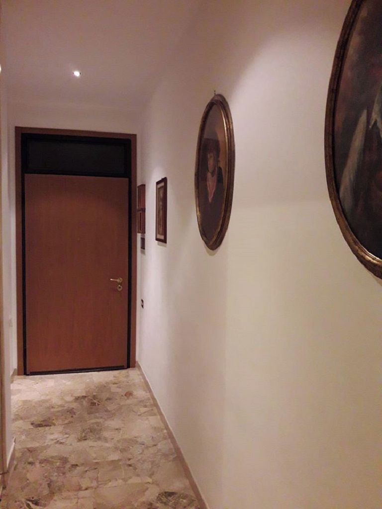 A hallway with a wooden door, framed pictures on the wall, and a stone floor.