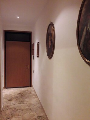 A hallway with a wooden door, framed pictures on the wall, and a stone floor. - Santo Spirito 2 (Arezzo)