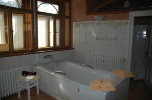 Une salle de bain avec une baignoire, une fenêtre avec des rideaux, un radiateur et un porte-serviettes.