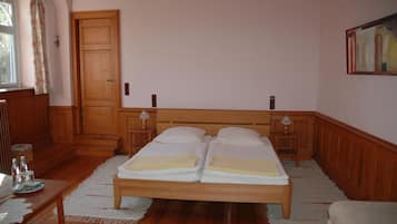 Ein Doppelbett mit zwei Kissen, ein Holz-Kopfteil, ein Nachttisch mit Lampe, ein Holzschrank und ein Fenster mit Vorhang.