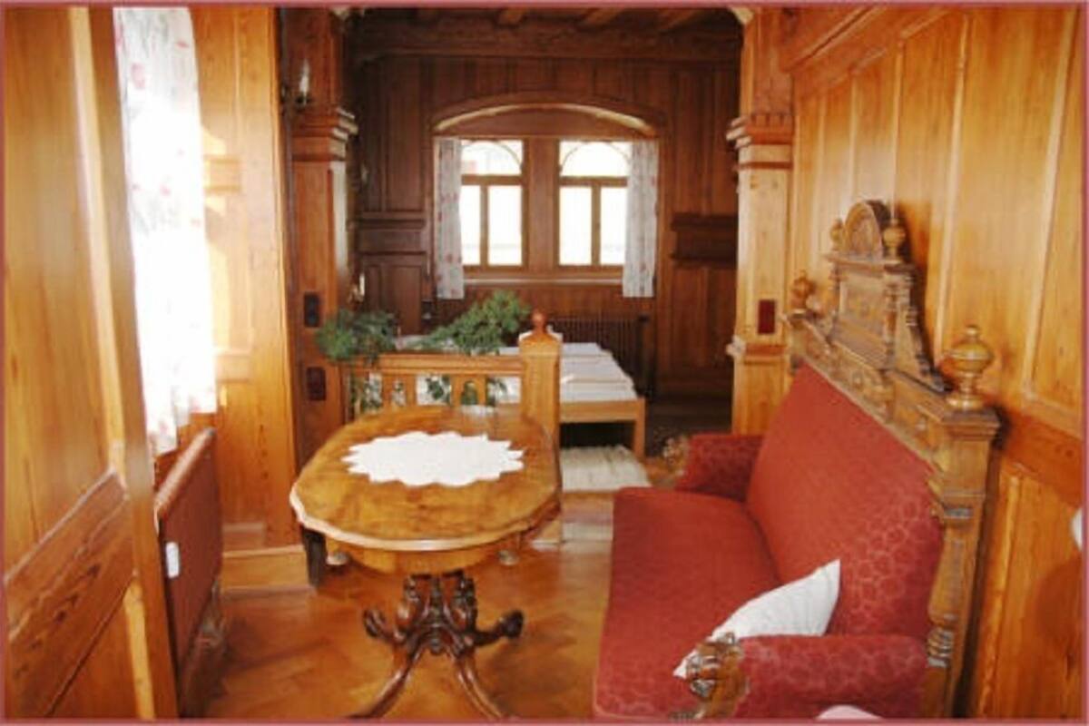 Ett rum med träpanel på väggarna, ett runt bord, en soffa och ett fönster med gardiner.
