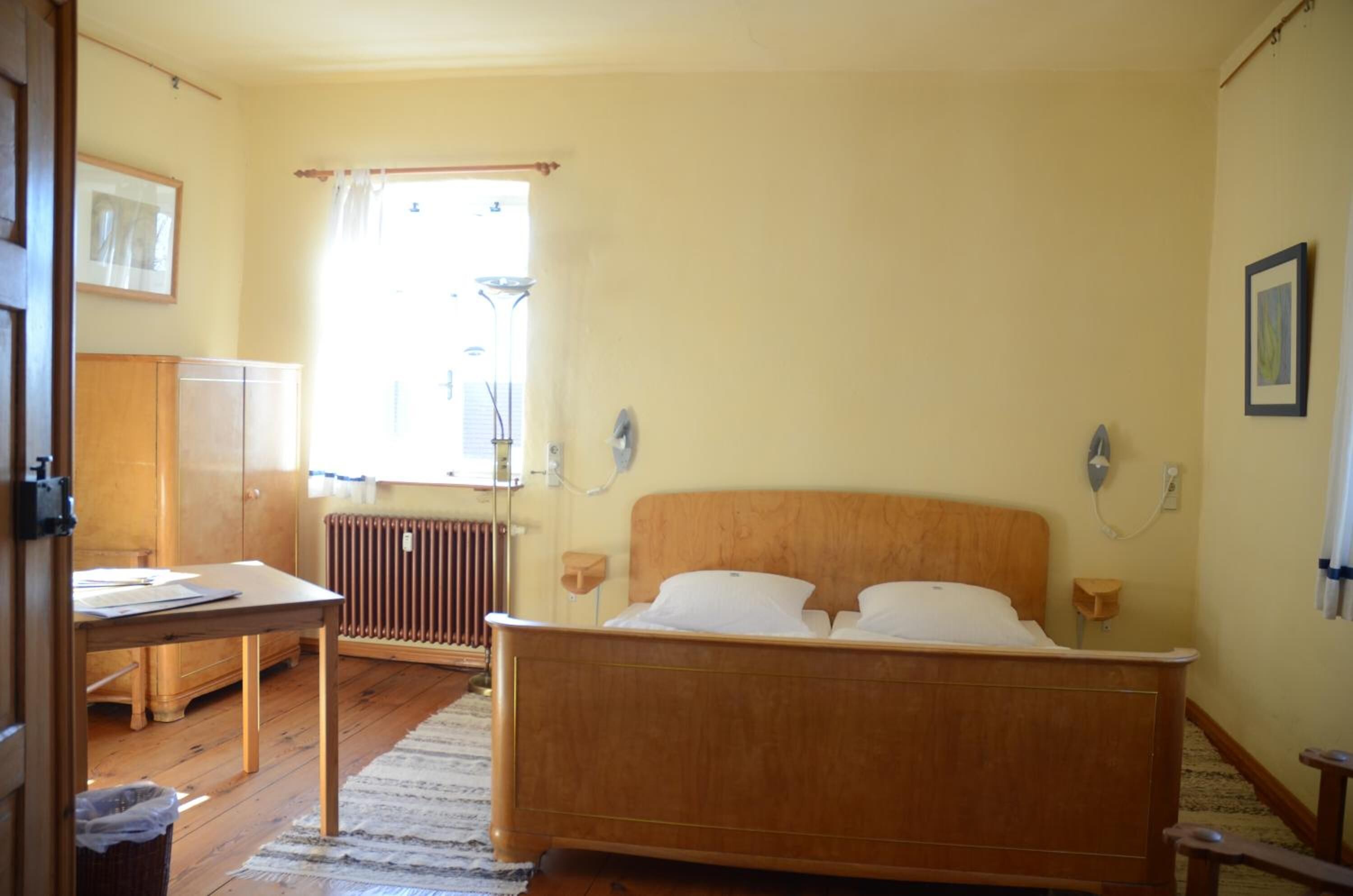 Ein Schlafzimmer mit einem hölzernen Bett, einem Heizkörper, einem Tisch und einem Fenster mit Vorhängen.