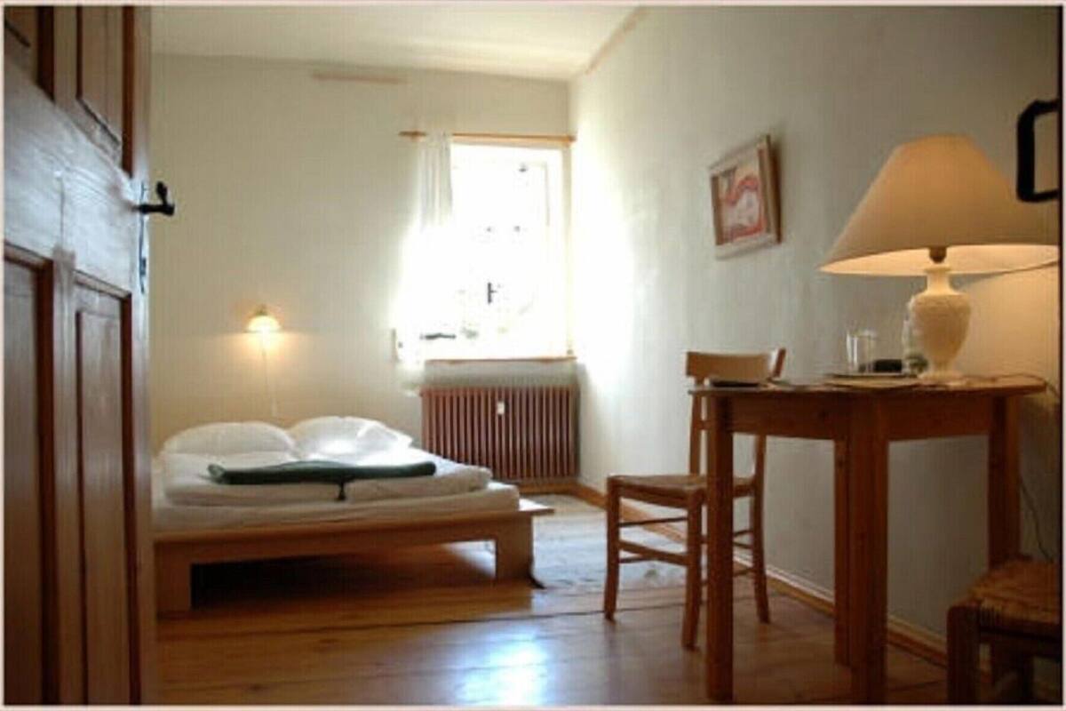Ett rum med en säng, ett bord med en lampa, en stol, ett element och ett fönster med gardiner.