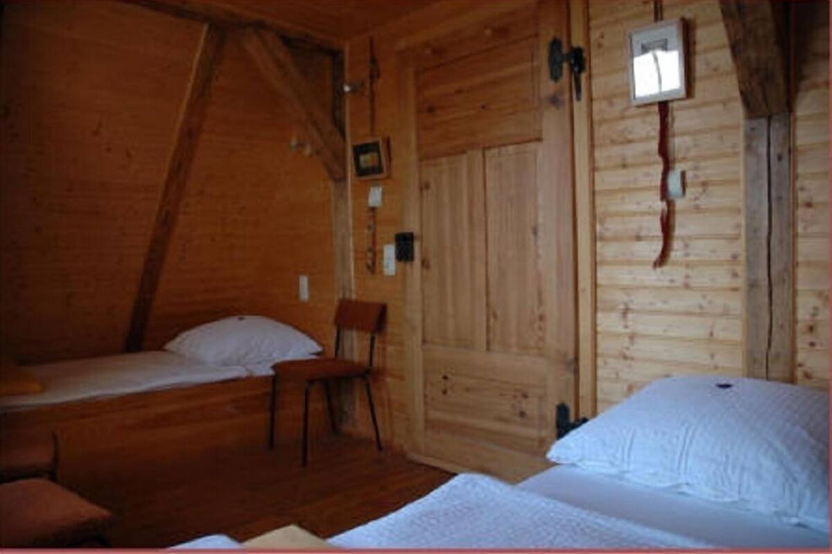 En stuga av trä med två sängar, en stol och ett litet bord.