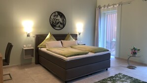 Une chambre à coucher comprenant un lit, deux tables de chevet, une œuvre d’art accrochée au mur, une fenêtre avec des rideaux et une petite plante en pot.