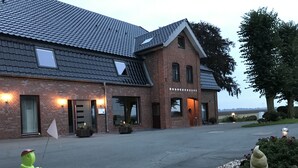 Un bâtiment en briques avec un toit en pente, de grandes fenêtres et une allée menant à l’entrée.