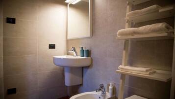 A bathroom with a pedestal sink, a mirror, and a towel rack with folded towels.