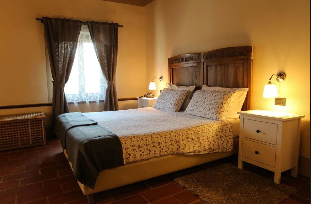 Una camera da letto con un letto, due comodini con lampade, una panca e una finestra con tende.